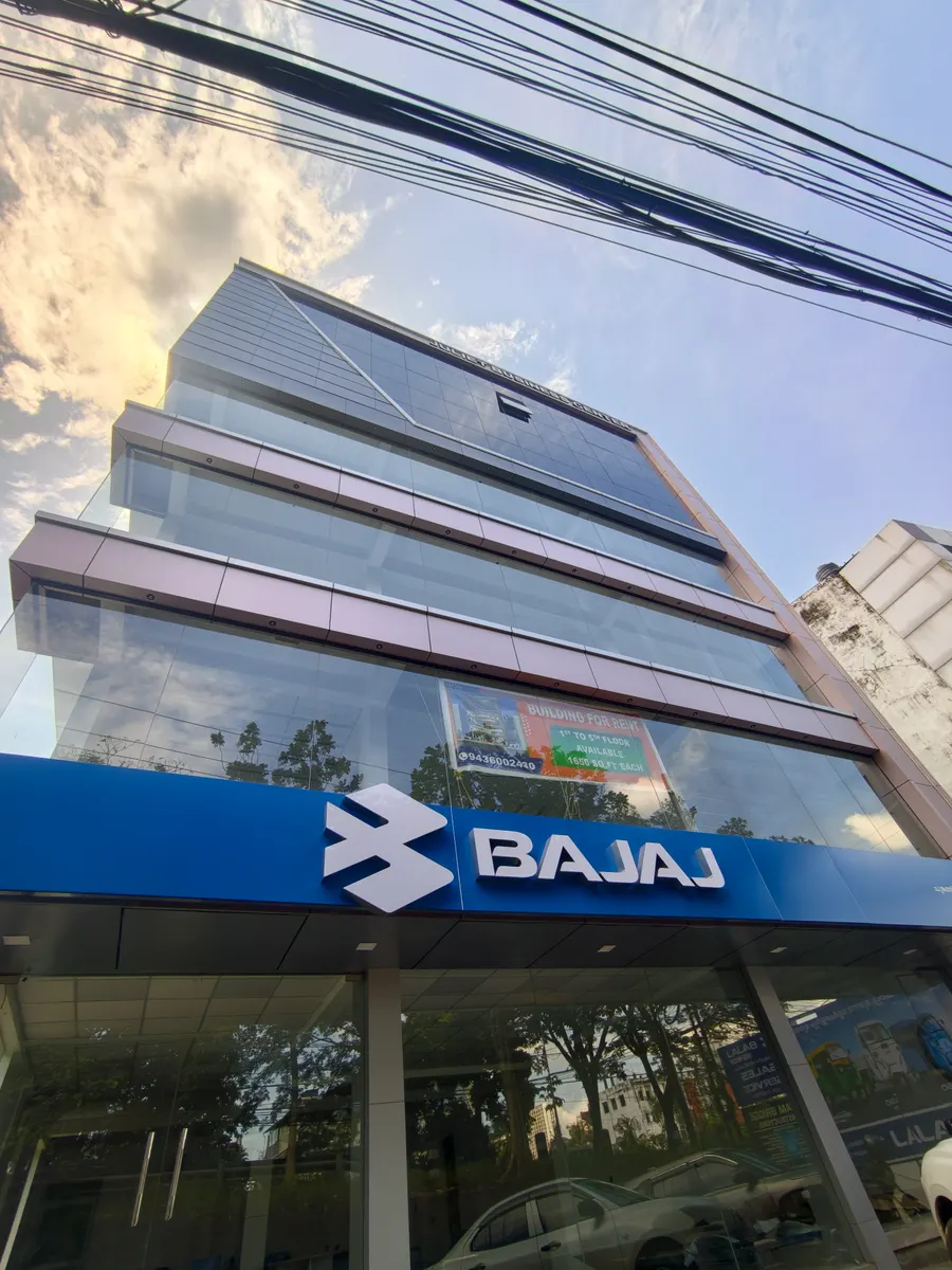 Glass-fronted multi-storey building with a blue Bajaj showroom sign at street level