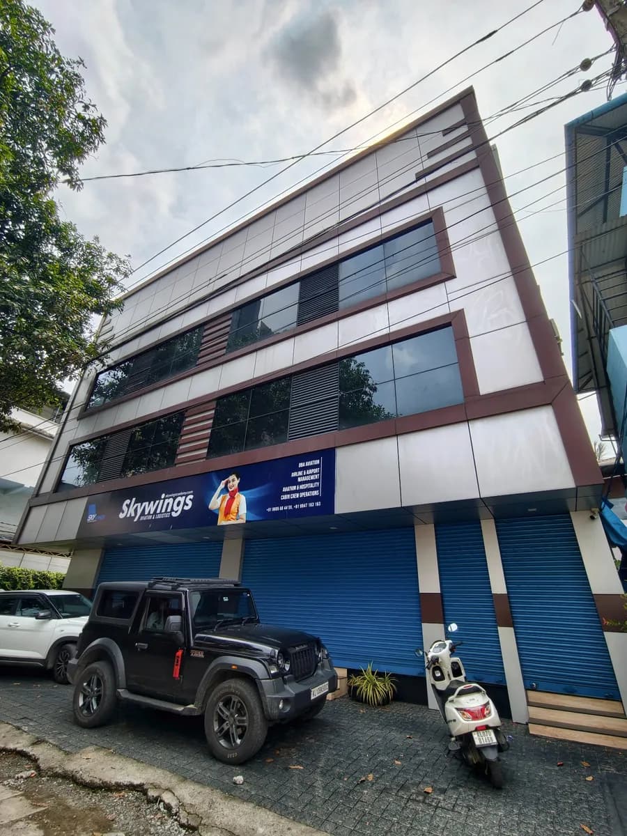 Four-storey commercial building at Chakkarapparamb with a blue signboard and blue shutters, vehicles in front