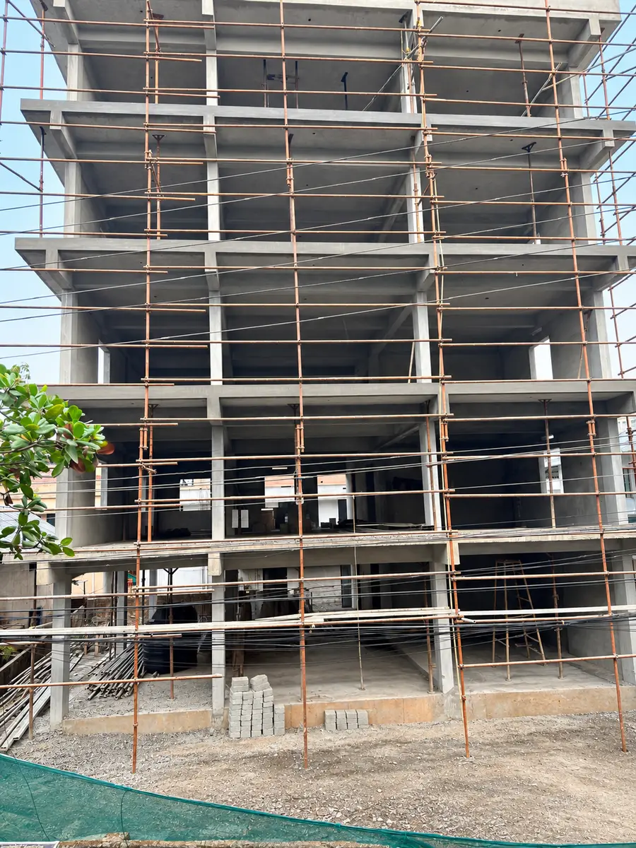 Multi-storey concrete frame covered in scaffolding, with a stack of paving blocks and gravel in front and a green net at the lower left