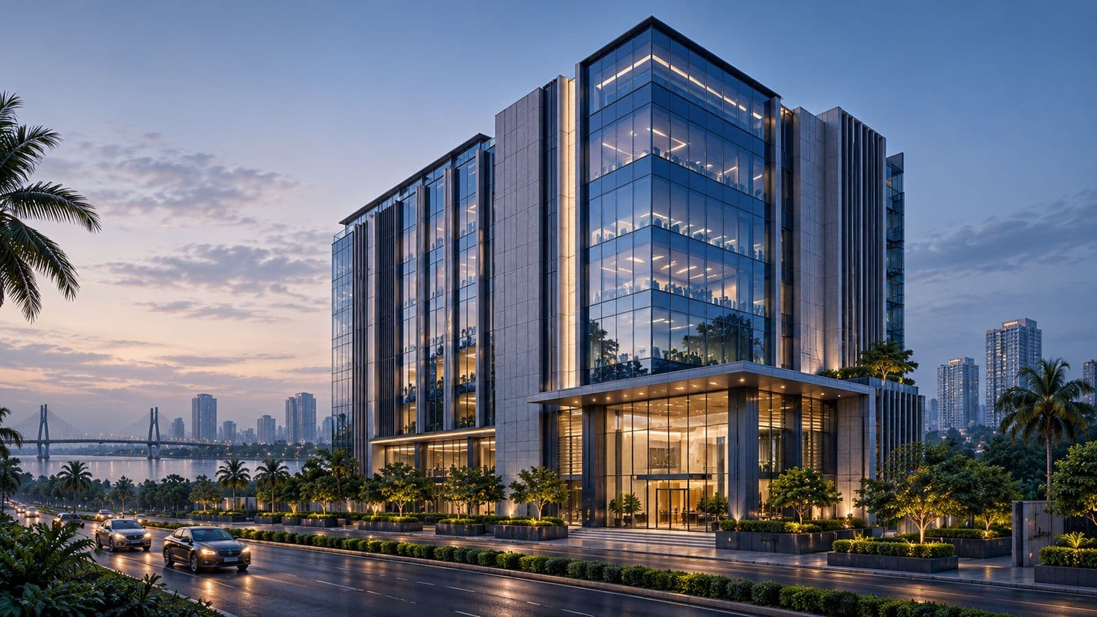 Modern glass office tower at dusk with a lit lobby, palm trees and a river bridge in the background